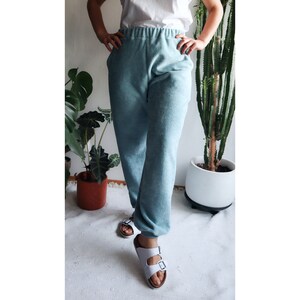 May include: A person wearing a pair of light blue sweatpants with a white top and white sandals.