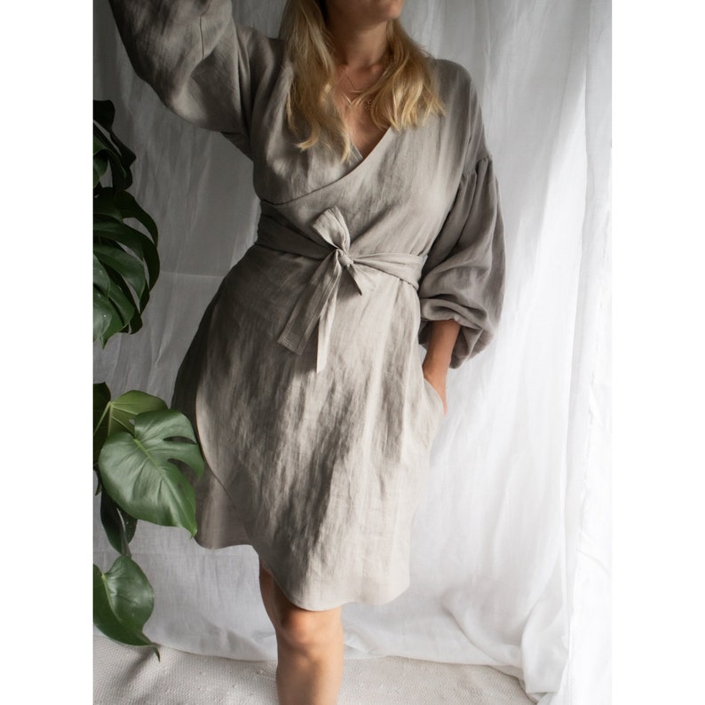 May include: A light gray linen wrap dress with a long sleeve and a tie at the waist.