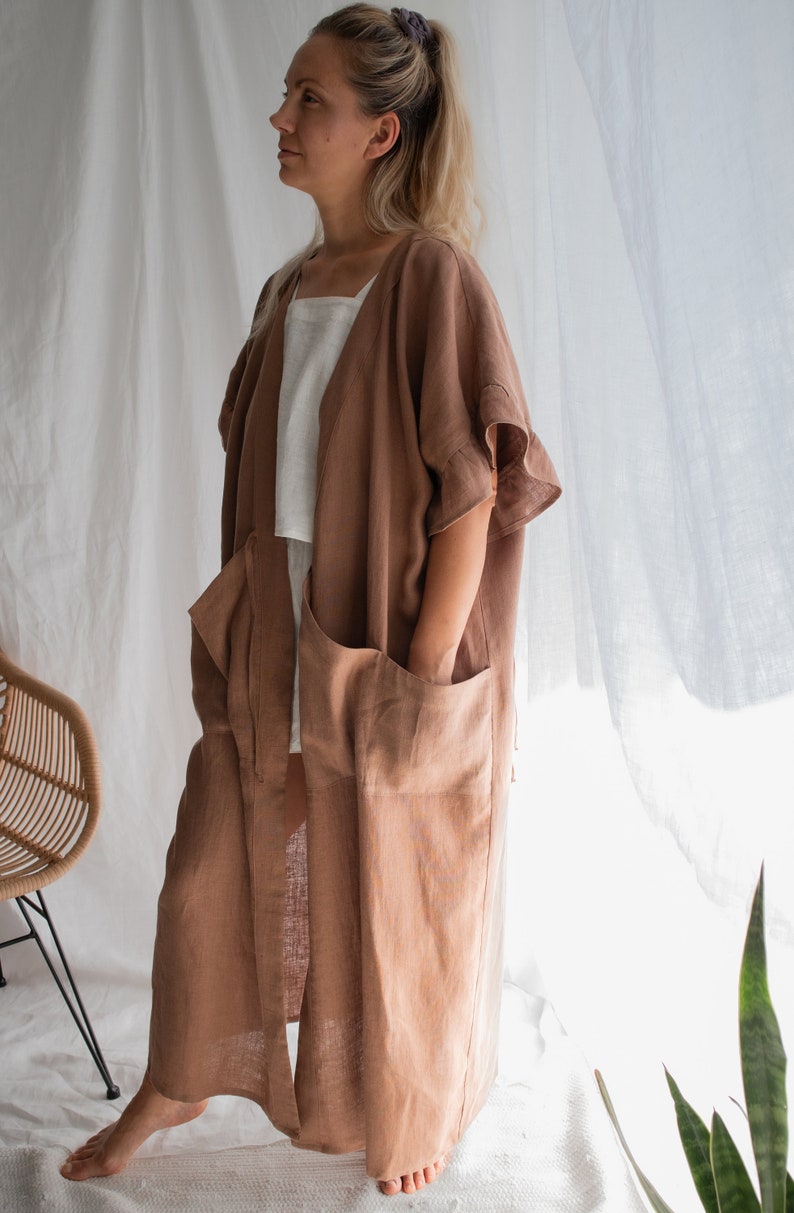 May include: A long, brown linen robe with a shawl collar, long sleeves, and two large pockets. The robe is open in the front and has a tie belt.