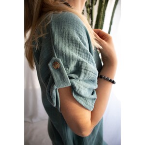 Puede incluir: Una camisa de gasa de algod&oacute;n azul turquesa con un bot&oacute;n en la manga. La camisa tiene un corte holgado y un estilo casual.
