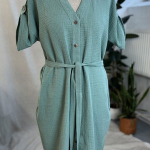 Puede incluir: Un vestido verde claro de manga corta con botones y cintur&oacute;n de lazo. El vestido tiene cuello en V y un corte holgado.