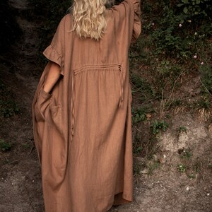 May include: A long, brown linen dress with a ruffled neckline and a drawstring waist. The dress is flowing and has a relaxed fit.