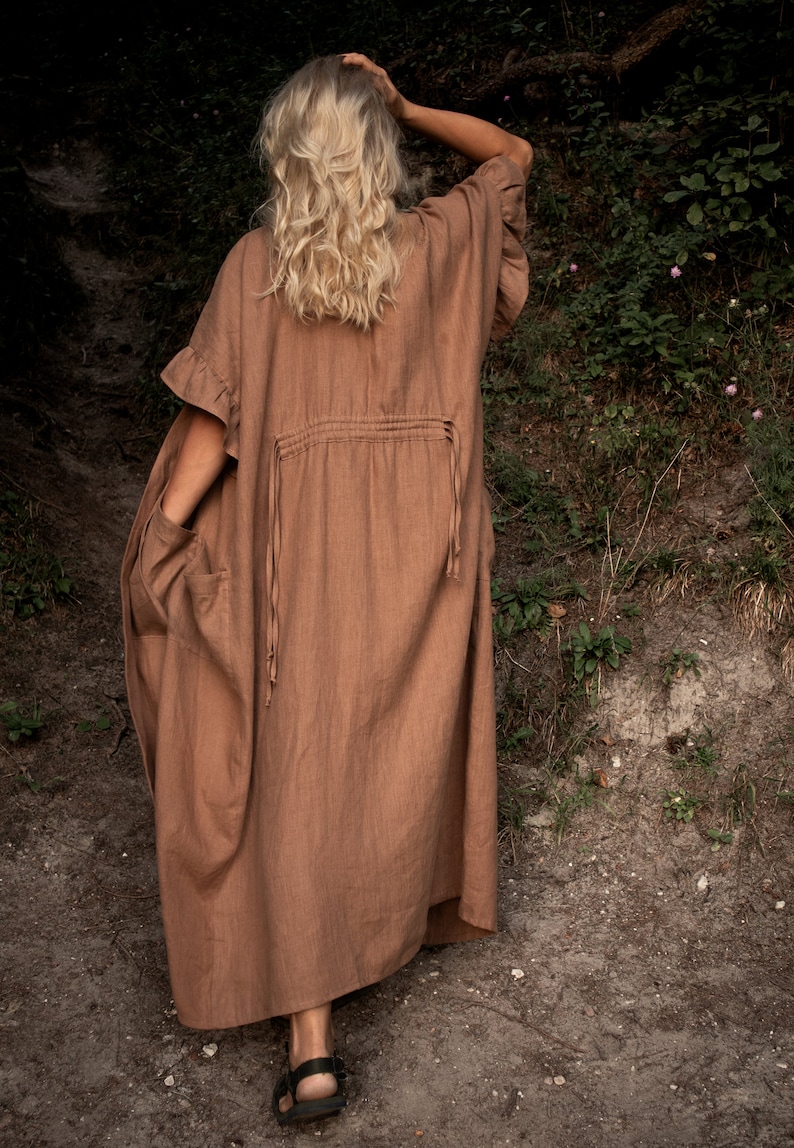May include: A long, brown linen dress with a ruffled neckline and a drawstring waist. The dress is flowing and has a relaxed fit.