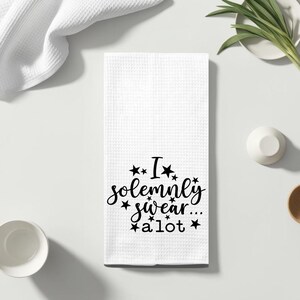 May include: White kitchen towel with black text that reads "I solemnly swear... a lot" with stars around the text.