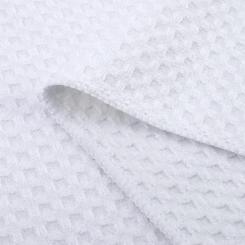 Puede incluir: Toalla de cocina blanca de tejido de gofre. La toalla est&aacute; doblada por la mitad y la textura del tejido es visible.