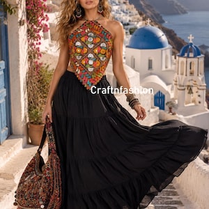May include: A sleeveless halter top featuring a multi-colored diamond-patterned embroidery with small circular mirrors, paired with a solid black tiered maxi skirt and a matching embroidered shoulder bag with dangling decorative accents.
