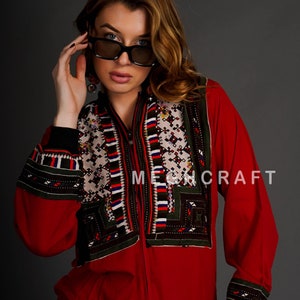 Peut inclure: Une veste rouge zippée avec des bordures noires et des détails brodés complexes dans des tons de vert, blanc et noir. La veste présente un col montant et des manches longues. Le texte "MECHCRAFT" est visible sur le devant de la veste.