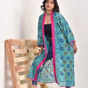 Peut inclure: Un long kimono bleu turquoise avec des bordures roses et des broderies complexes. Le kimono est orné de décorations en forme de miroir et présente un motif floral.