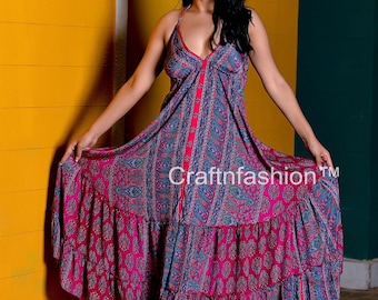 May include: A woman wearing a long, flowing, pink and blue floral print maxi dress with a halter neckline and a button-up front. The dress has a tiered skirt and is made of a lightweight fabric.