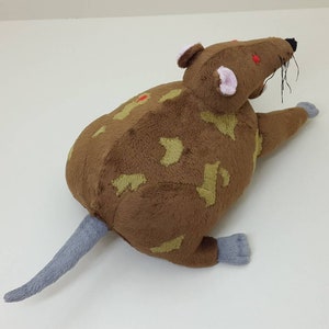 K&ouml;nnte beinhalten: Ein braunes und hellbraunes Pl&uuml;schrat mit roten Augen und einem grauen Schwanz. Die Ratte liegt auf der Seite mit dem Kopf zur Seite gedreht.