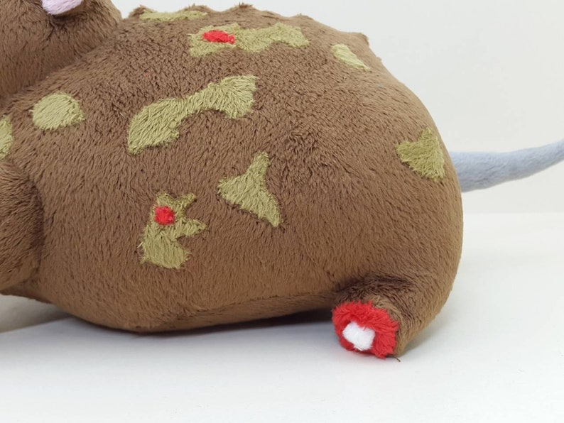 K&ouml;nnte beinhalten: Braunes Pl&uuml;schtier mit einem grauen Schwanz und gr&uuml;nen und roten Stickdetails. Das Spielzeug hat die Form einer Ratte oder Maus.
