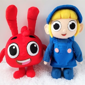 May include: A red plush toy with large eyes and bunny ears, standing next to a blue plush toy with a yellow hat and blonde hair. Both toys have a cartoonish appearance.