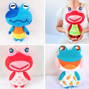 May include: Four plush frog toys, two blue and two red. The blue frogs are wearing orange and yellow shirts, while the red frogs are wearing green and white dresses. The frogs have big eyes and smiles.