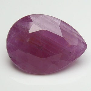 May include: A pear-shaped, faceted ruby gemstone with a deep pink hue. The gemstone is set against a white background.