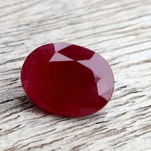 Op de afbeelding: Een dieprode edelsteen met een facetgeslepen vorm, liggend op een licht houten oppervlak.