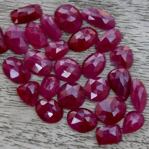 Puede incluir: Una colección de 20 piedras preciosas de rubí facetadas de diferentes tamaños y formas. Los rubíes son de color rojo intenso y tienen un acabado pulido y facetado.