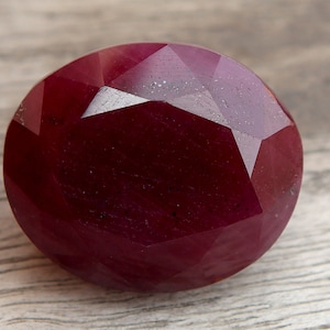 Puede incluir: Una piedra preciosa de rubí rojo oscuro con un corte facetado. La piedra preciosa es redonda y tiene un acabado pulido.