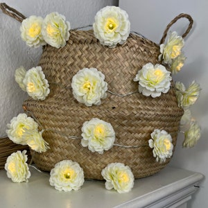 May include: A string of white flower lights wrapped around a woven basket. The lights are on and emit a warm glow.