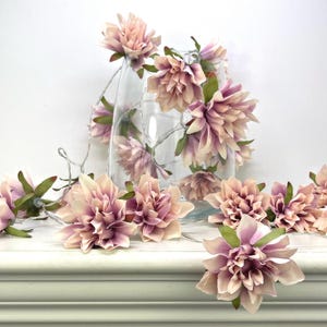 May include: A string of fairy lights adorned with delicate pink and white faux dahlia flowers. The lights are wrapped around a clear glass vase, ideal for adding a touch of whimsy to any space.