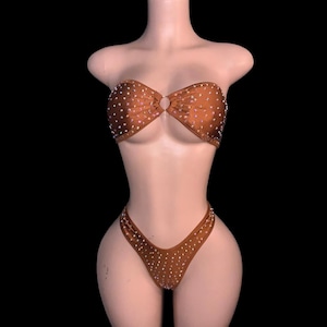 May include: A brown bikini set with sparkling embellishments. The strapless top has a central ring detail, and the bottoms have a high-cut design. The bikini is displayed on a mannequin against a black background.