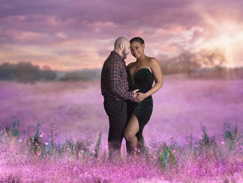 May include: A pregnant woman wearing a green velvet dress and a man in a checked shirt stand in a field of purple flowers. They are looking at each other and smiling.