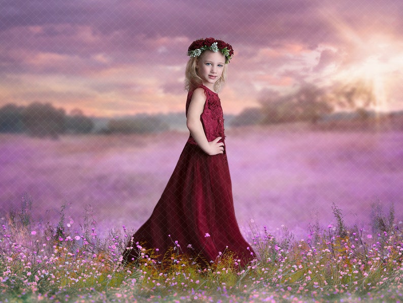 May include: A young girl wearing a red dress and a flower crown stands in a field of purple flowers. The sky behind her is a soft purple and pink.
