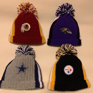 May include: Four crocheted hats with team logos. The hats are red, purple, gray, and black with white and yellow stripes. The logos are the Washington Redskins, Baltimore Ravens, Dallas Cowboys, and Pittsburgh Steelers.