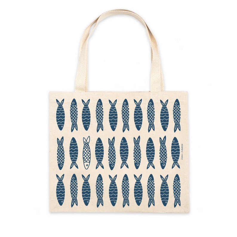 May include: A beige tote bag with blue fish illustrations printed on the front. The fish are all facing the same direction and have a simple, stylized design.