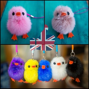 May include: Six fluffy pom-pom keychains shaped like chicks in various colors, including pink, purple, yellow, blue, white, and black. Each keychain has a small orange beak and feet.