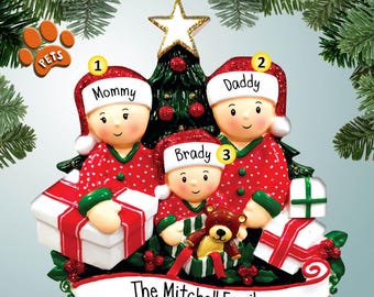 May include: A Christmas ornament featuring a family of three in pajamas, standing in front of a decorated Christmas tree. The ornament is personalized with the names "Mommy", "Daddy", and "Brady" and the text "The Mitchell Family".