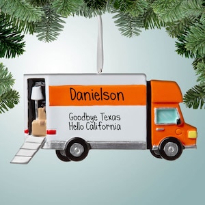 May include: Orange and white moving truck Christmas ornament with the name "Danielson" and the text "Goodbye Texas Hello California".