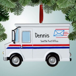 May include: White mail truck Christmas ornament with red, white, and blue stripes. The ornament has the name "Dennis" and "Seattle Post Office" written on it.