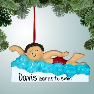 May include: A personalized Christmas ornament featuring a boy swimming in blue water. The ornament is white with the text "Davis learns to swim".