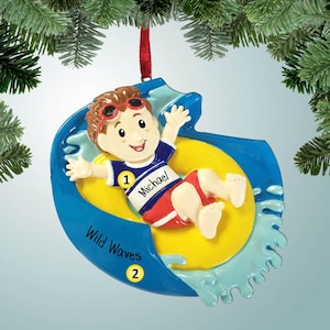 May include: A blue and yellow Christmas ornament depicting a boy wearing red shorts and a blue shirt with the name "Michael" on it. The boy is riding a yellow inner tube down a blue waterslide. The ornament says "Wild Waves" and has the number "2" on it.