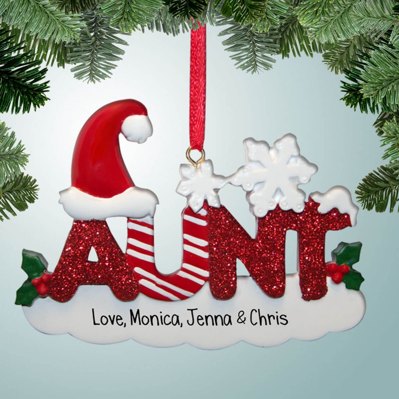 K&ouml;nnte beinhalten: Roter Glitzer-Weihnachtsbaumschmuck mit dem Wort "TANTE" in wei&szlig;en Buchstaben. Das "A" hat einen Weihnachtsmann-Hut oben drauf und das "U" hat einen Zuckerstangen-Streifen. Der Schmuck hat oben einen wei&szlig;en Schneeflock und eine wei&szlig;e Wolkenbasis mit dem Text "Love, Monica, Jenna & Chris".