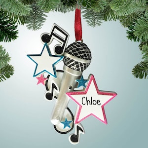 May include: A silver microphone Christmas ornament with a black mesh head, surrounded by white stars with blue and pink glitter trim, and black musical notes. The name "Chloe" is written on a pink star.