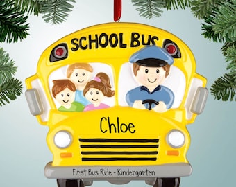 Könnte beinhalten: Gelber Schulbus-Weihnachtsbaumschmuck mit einem lächelnden Busfahrer und Kindern im Inneren. Der Schmuck ist mit dem Namen "Chloe" und dem Text "Erste Busfahrt - Kindergarten" personalisiert.