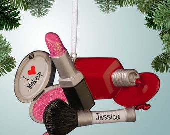 Könnte beinhalten: Ein Weihnachtsbaumschmuck in Form von Make-up-Artikeln, darunter Lippenstift, Nagellack und Make-up-Pinsel. Der Schmuck ist mit Glitzer verziert und hat ein pinkfarbenes Herz mit dem Text "Ich liebe Make-up" darauf. Der Schmuck hat auch ein weißes Etikett mit dem Namen "Jessica" darauf.