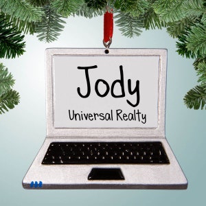 May include: Silver laptop bauble with a white screen that says "Jody Universal Realty". The bauble has a red ribbon attached to the top.