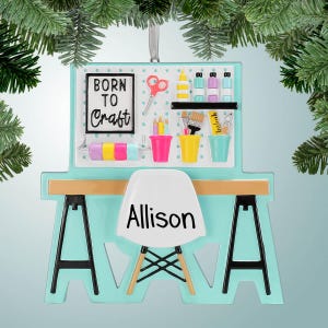 May include: A turquoise blue craft table ornament with a white chair. The table has a pegboard with paint tubes, paintbrushes, pencils, and a sign that says "Born to Craft". The chair has the name "Allison" written on it.