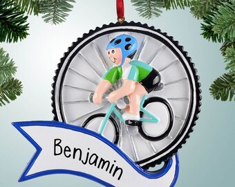 May include: A personalized Christmas ornament featuring a blue and green cyclist riding a bicycle with a silver wheel. The ornament has a blue and white banner with the name "Benjamin" written on it.