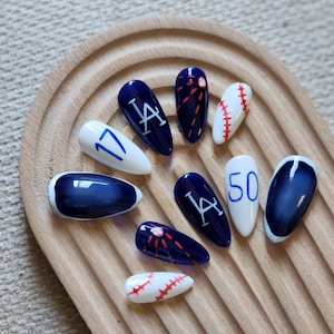 May include: A set of ten almond-shaped press-on nails featuring a baseball theme with navy blue and white colors. Designs include the LA logo, the numbers 17 and 50, red baseball stitching patterns, and small baseball illustrations.