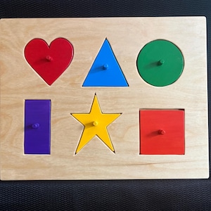 May include: A rectangular wooden puzzle board featuring six colorful geometric shapes: a red heart, a blue triangle, a green circle, a purple rectangle, a yellow star, and a red square. Each shape includes a small wooden peg for easy handling.