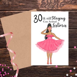May include: Greeting card with a drawing of a woman in a pink dress and the text "30 & still Slaying Con Actitud Latina". The card is on a wooden surface with a brown envelope and pink ribbon.