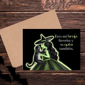 May include: Greeting card with a witch illustration holding a black cat, with the text "Eres mi bruja favorita y tu gato también." The witch is depicted with green skin and a black hat and dress. A brown envelope and bat silhouettes are also visible.