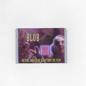 Op de afbeelding: Een rechthoekige verzamelkaart met een paarse en roze afbeelding uit de film The Blob. De kaart bevat de tekst THE BLOB en ACTUAL SWATCH OF BLOB FROM THE FILM, met een klein vierkant ingebed staaltje van roze materiaal in het midden.