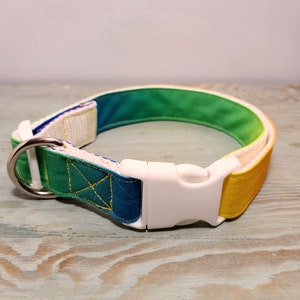 May include: A dog collar with a white plastic buckle and a metal D-ring. The collar features a gradient of colors, transitioning from yellow to green to blue. The collar is approximately 1 inch wide.
