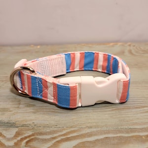 Puede incluir: Un collar de perro a rayas rosa y azul con una hebilla de plástico blanca.
