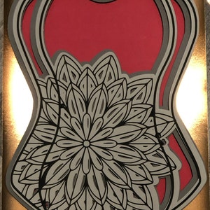 Könnte beinhalten: Ein mehrschichtiges Papierbastel-Design mit einem großen, filigranen Mandala in Schwarzweiß auf rotem Hintergrund.