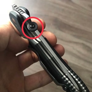 May include: Close-up of a black and silver pocket knife with a textured handle. A small black screw is visible on the side of the knife.